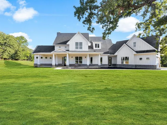 a view of a white house next to a yard with a large trees