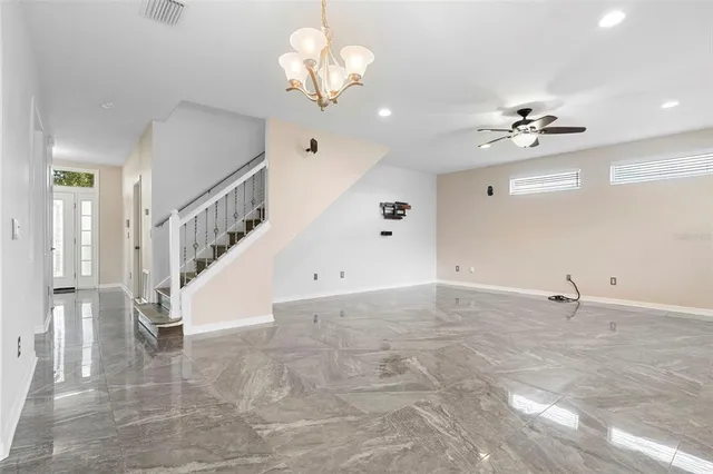 an empty room with chandelier fan and windows