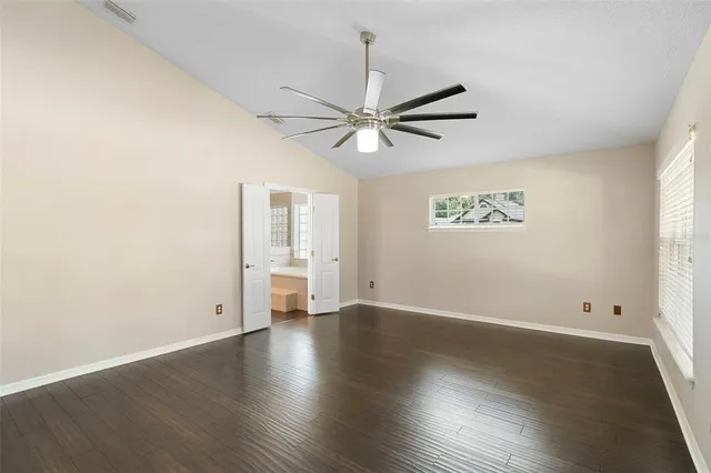 an empty room with wooden floor chandelier fan and windows