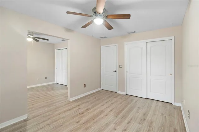 an empty room with wooden floor ceiling fan and windows