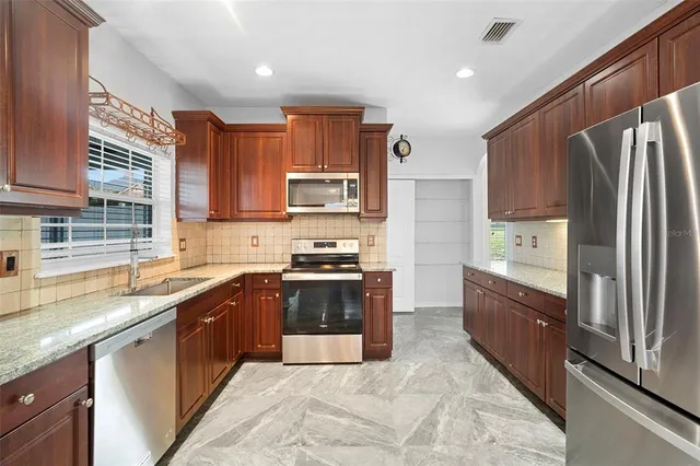 a large kitchen with stainless steel appliances granite countertop a stove top oven a sink and dishwasher a refrigerator with wooden cabinets