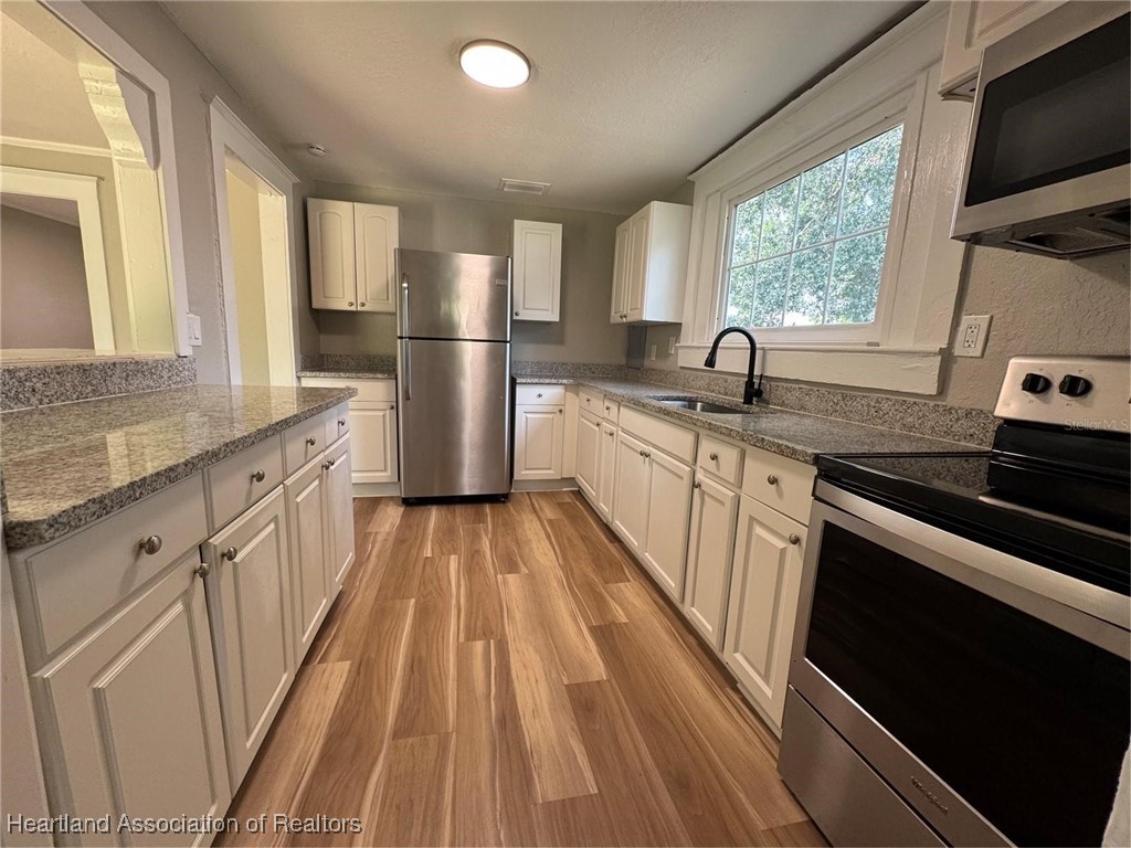 111 D Street Frostproof, FL 33843 - Photo 17 of 40 a kitchen with granite countertop a refrigerator a sink dishwasher a stove and white countertops with wooden floor