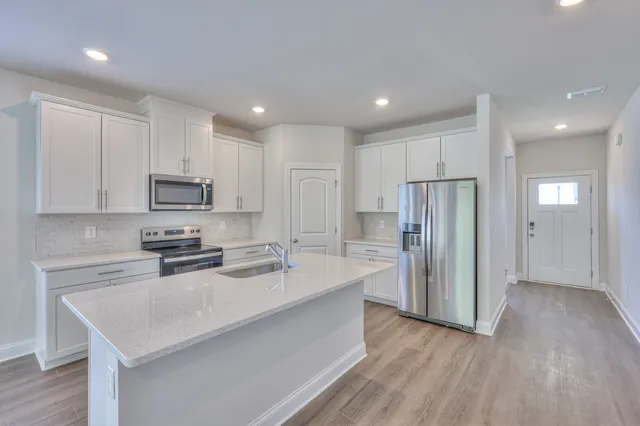 a kitchen with stainless steel appliances granite countertop a refrigerator a sink dishwasher a stove and white countertops with wooden floor