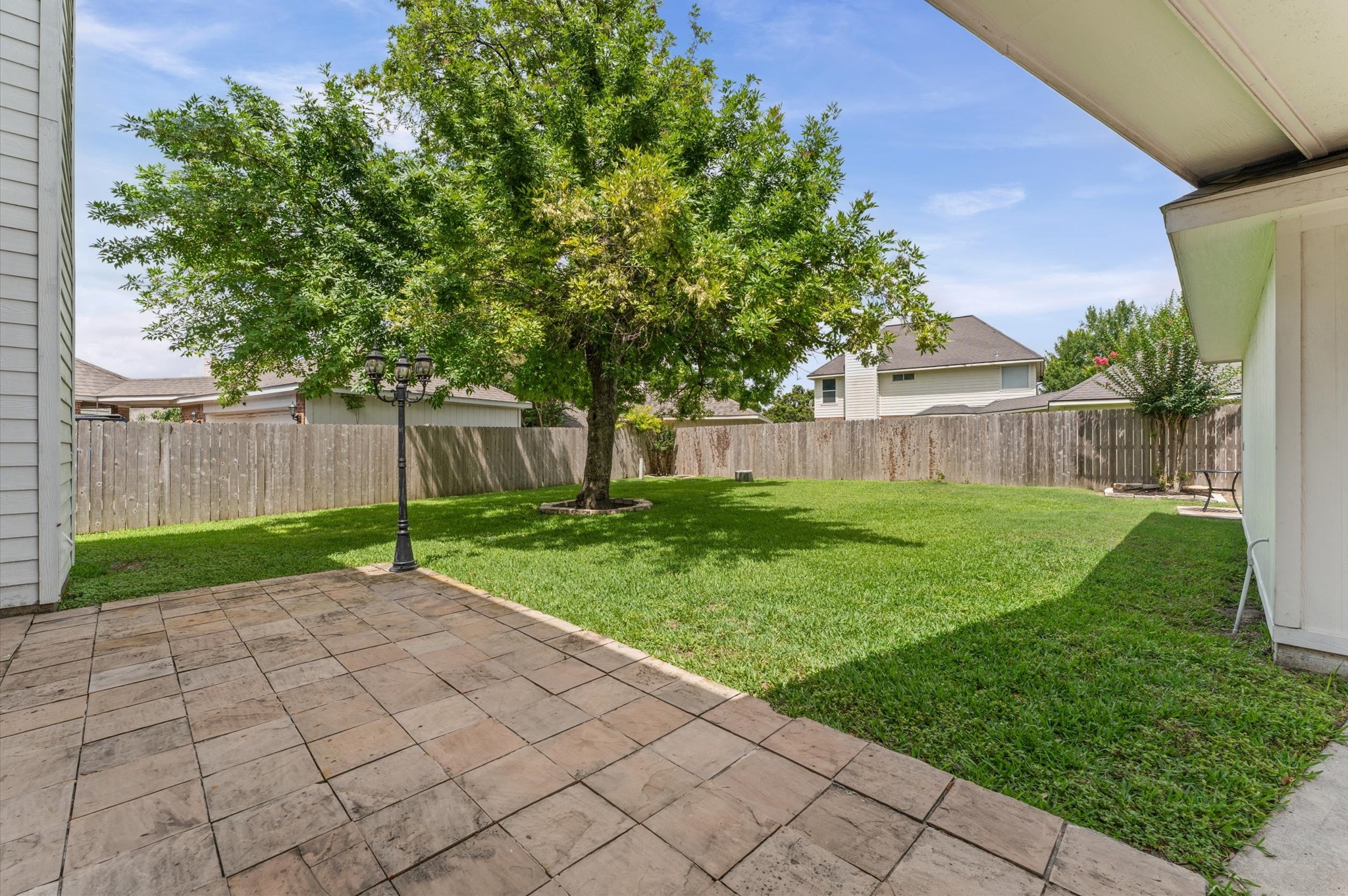 9202 State Walk Circle Houston, TX 77064 - Photo 22 of 25 This backyard features a spacious, well-maintained grassy area with a mature tree providing shade. A paved patio area is ideal for outdoor seating, and the space is enclosed by a wooden fence, offering privacy.