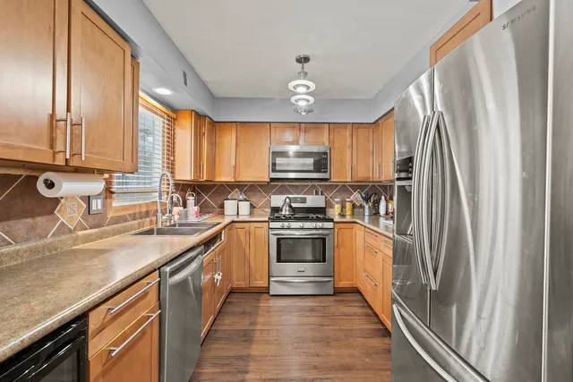 a kitchen with stainless steel appliances granite countertop a refrigerator a sink dishwasher a stove and white countertops with wooden floor