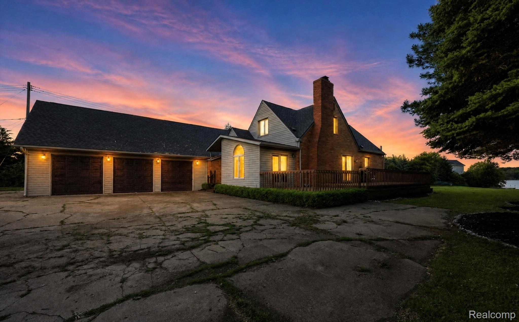 Property exterior featuring a three-car garage with dark wood-finish doors, a brick chimney, and a multi-level wood deck
