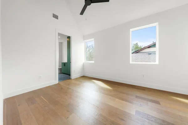 an empty room with wooden floor fan and windows