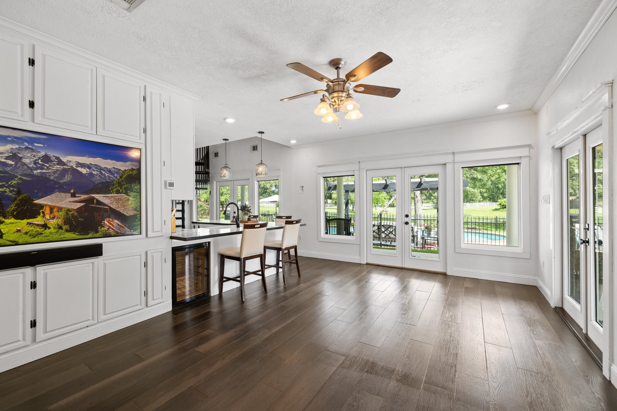 34310 High Point Drive Magnolia, TX 77355 - Photo 27 of 48 This spacious, bright living room in the guest house features elegant tile wood look floors and a ceiling fan. It opens to a scenic backyard with large windows and French doors, offering views of a pool and greenery. The open concept includes a modern kitchen with a breakfast bar and stylish lighting.