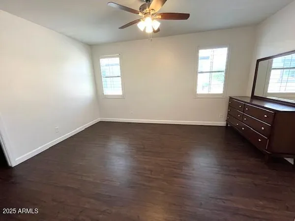 an empty room with wooden floor fan and windows