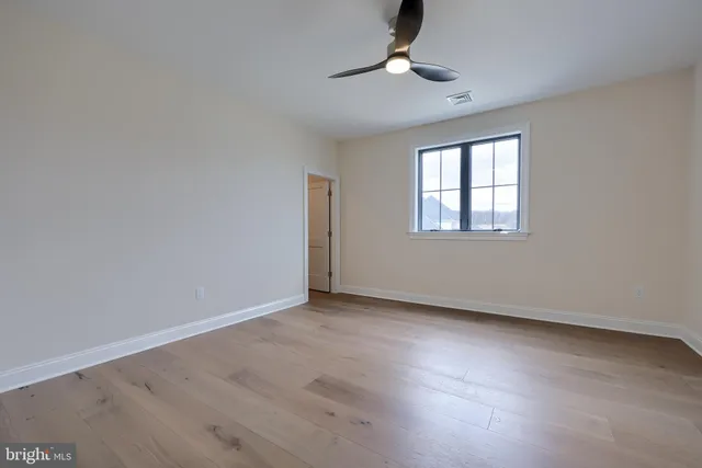 an empty room with wooden floor chandelier fan and windows