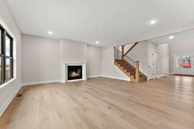 a view of an empty room with wooden floor staircase and a kitchen