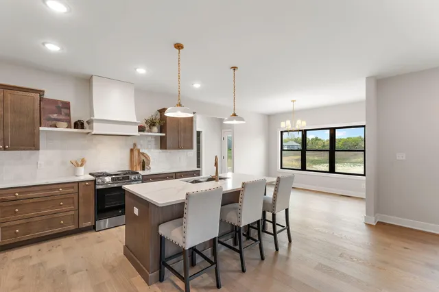 a kitchen with stainless steel appliances granite countertop a stove top oven a sink dishwasher a dining table and chairs with wooden floor