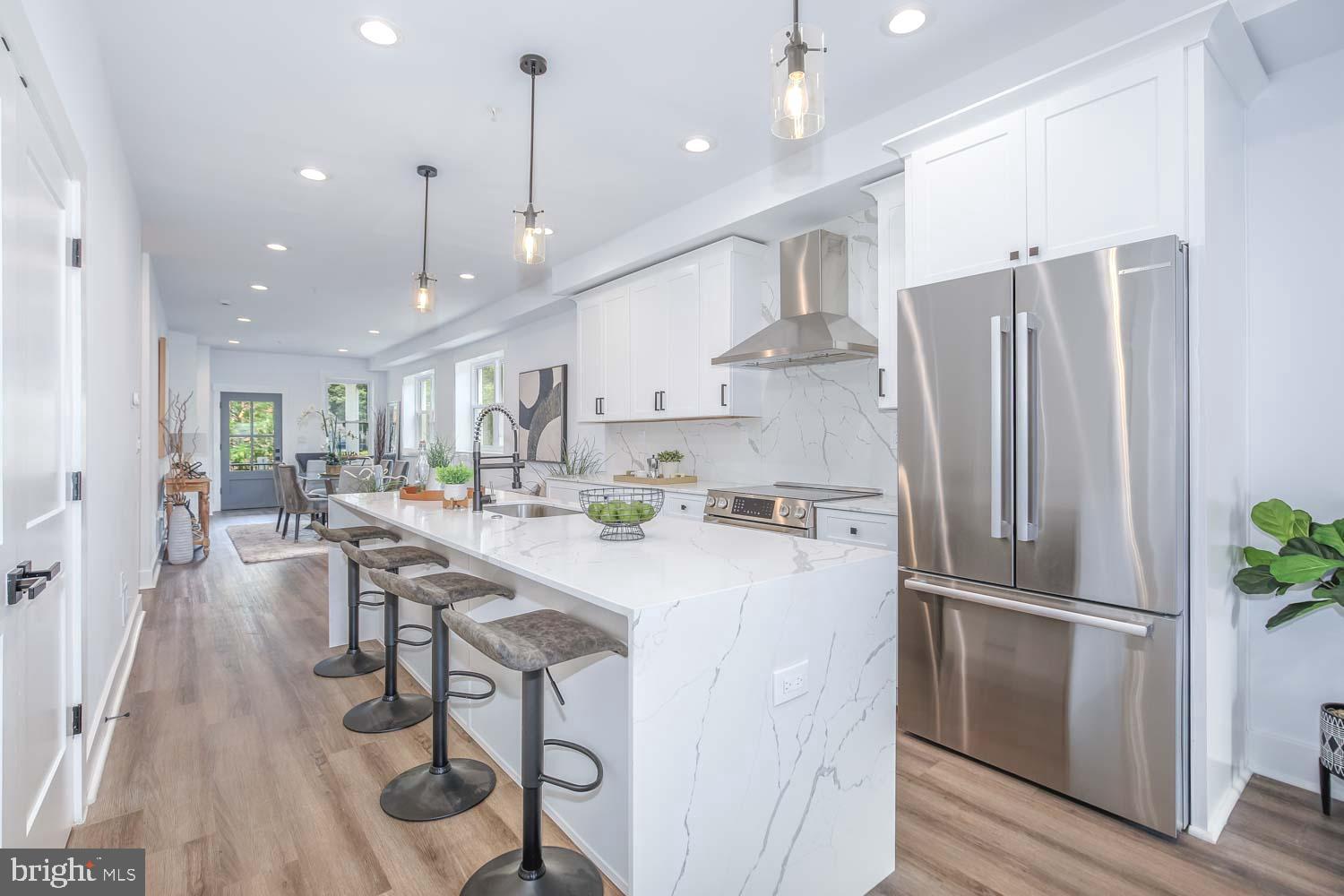 a kitchen with stainless steel appliances granite countertop a refrigerator a sink dishwasher a stove a dining table and chairs with wooden floor