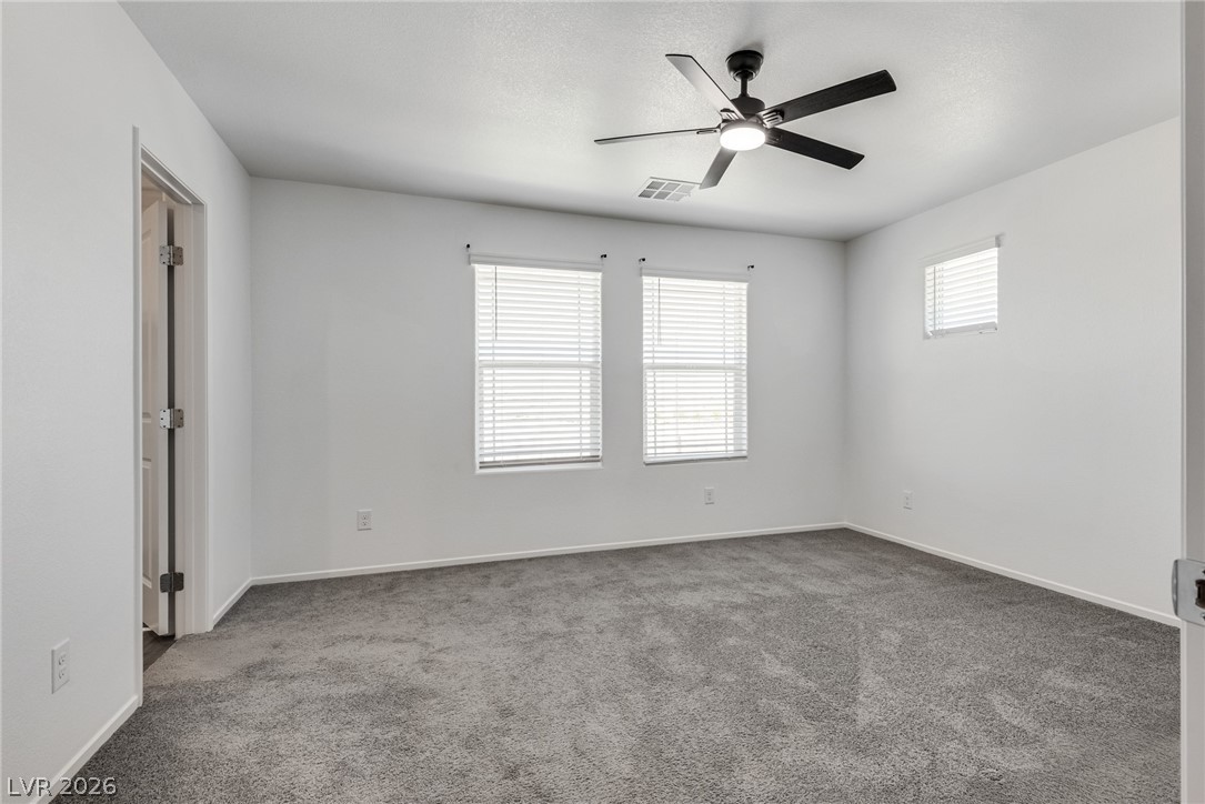 1114 Scarlet Sparrow Street Henderson, NV 89011 - Photo 14 of 25 A well-lit bedroom features plush carpeting and a ceiling fan, offering a comfortable retreat.