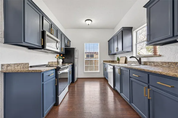 a kitchen with stainless steel appliances granite countertop a sink a stove a microwave cabinets and a window