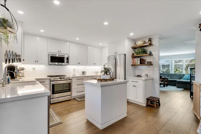 a kitchen with stainless steel appliances granite countertop a refrigerator a stove top oven a sink dishwasher and white cabinets with wooden floor