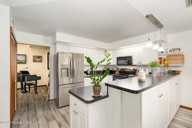 a kitchen with stainless steel appliances granite countertop a refrigerator a sink dishwasher a stove a dining table and chairs with wooden floor