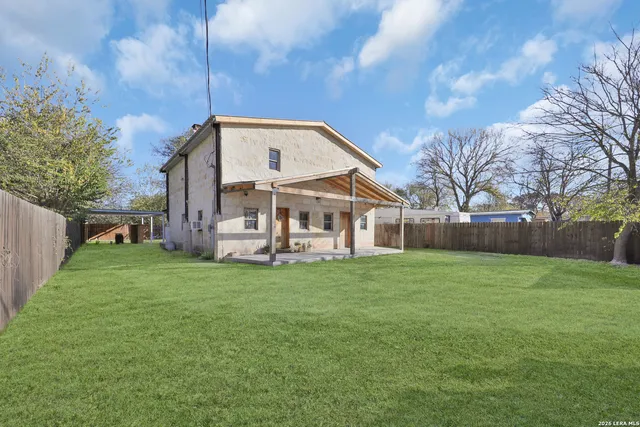 a view of a house next to a big yard with plants and large trees