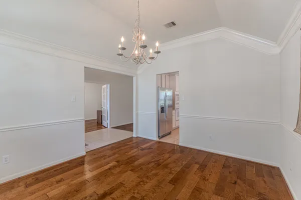 a large kitchen with granite countertop a stove a sink a refrigerator and white cabinets with wooden floor