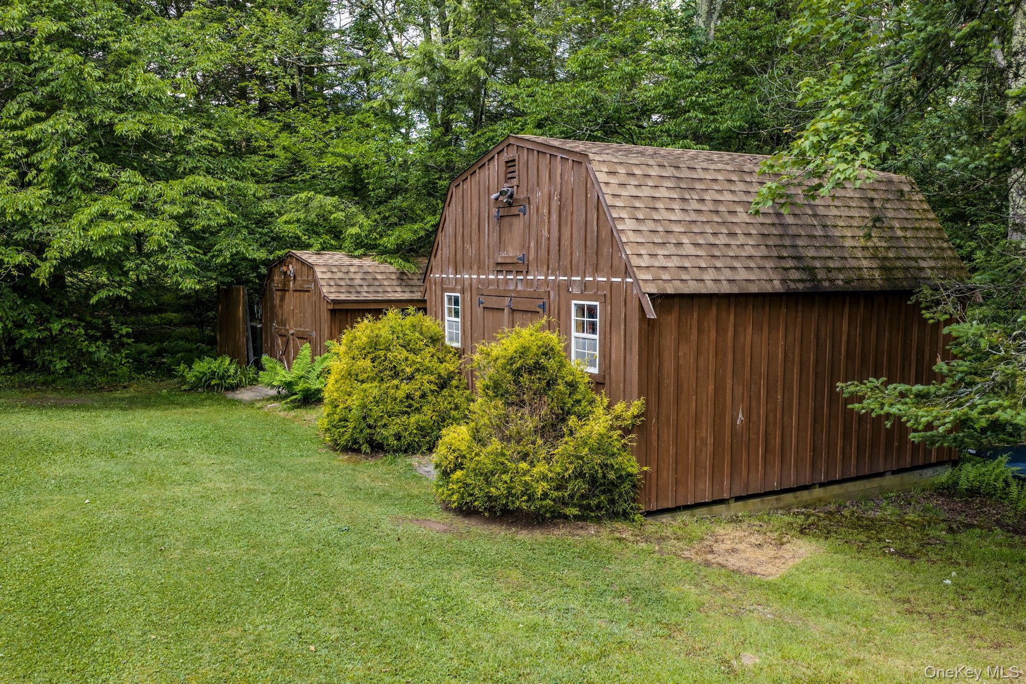 172 Wards Road Livingston Manor, NY 12758 - Photo 44 of 47 Brown-stained wood siding barn with gambrel roof and white-framed windows, accompanied by a smaller coordinating shed