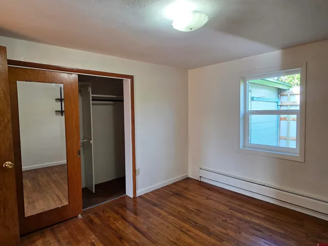 an empty room with wooden floor closet and windows
