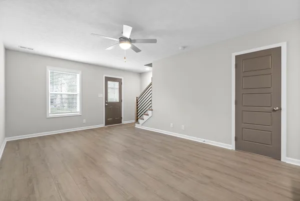 a view of an empty room with wooden floor and a ceiling fan
