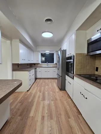 a kitchen with stainless steel appliances granite countertop a refrigerator a stove top oven a sink dishwasher and white cabinets with wooden floor