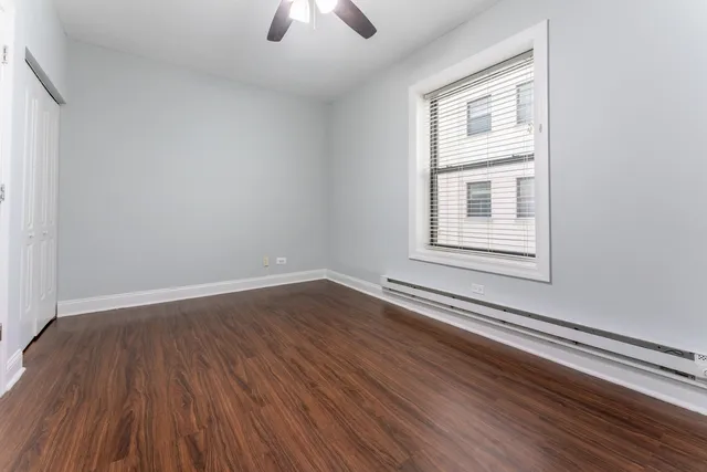 an empty room with wooden floor chandelier fan and windows
