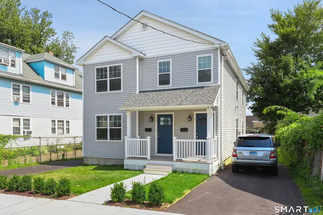 a view of a white house next to a yard with plants and trees