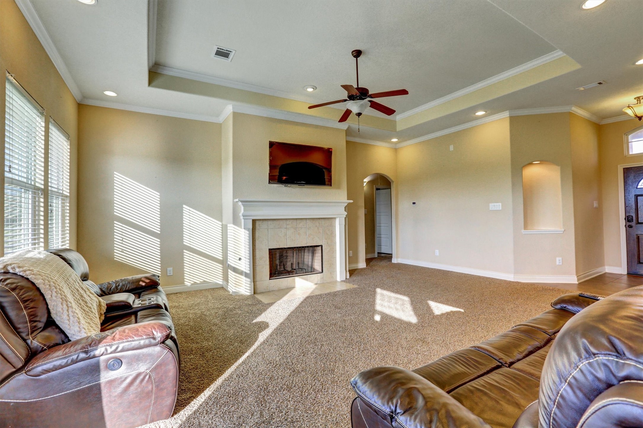 8131 Brinkmeyer Road Needville, TX 77461 - Photo 49 of 49 Spacious living room with a cozy fireplace, tray ceiling, and abundant natural light, perfect for relaxation and entertaining.