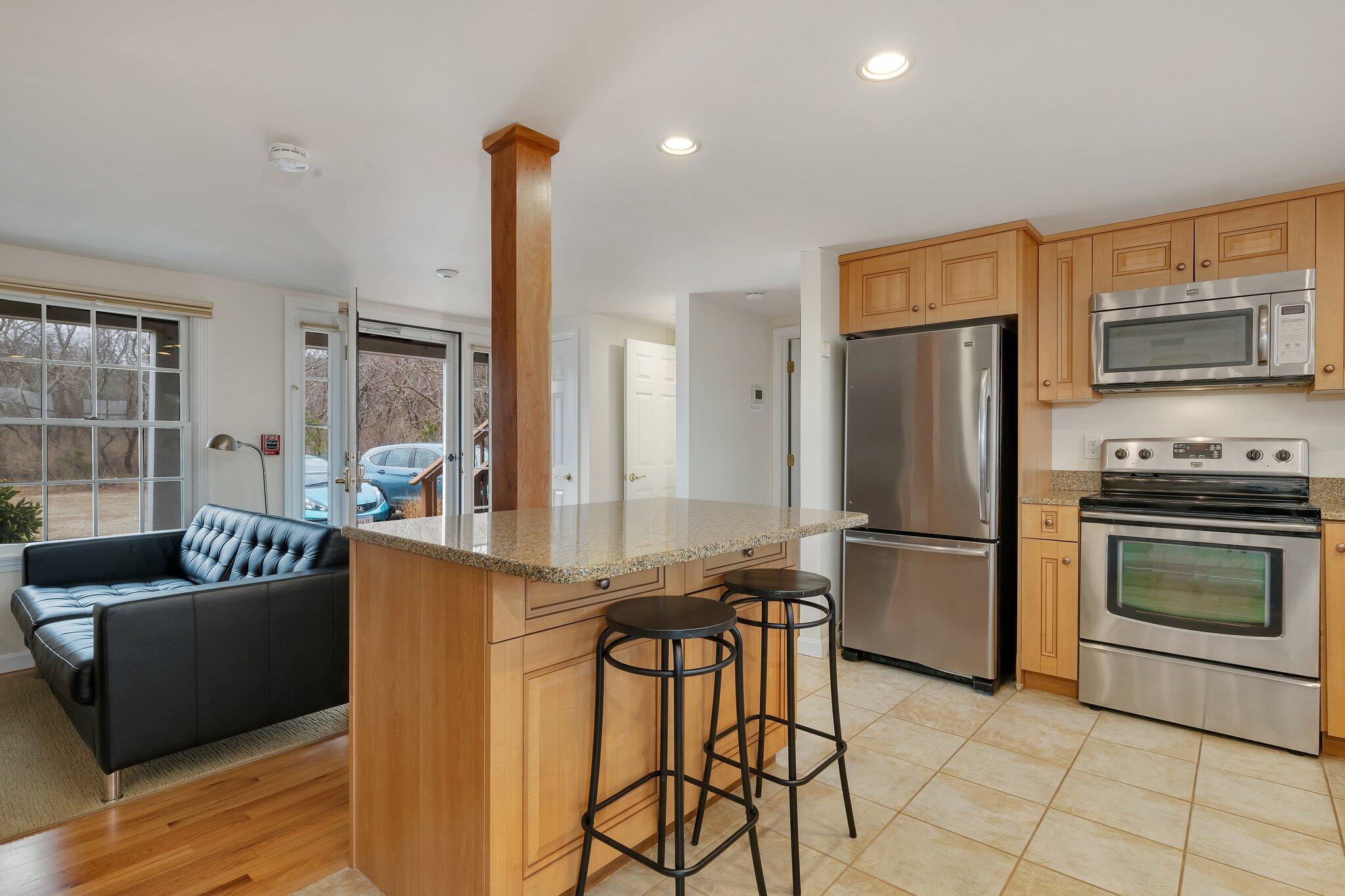6 Shore Road, Unit 26 Truro, MA 02666 - Photo 5 of 25 a kitchen with stainless steel appliances kitchen island granite countertop a refrigerator a stove a microwave a dining table and chairs with wooden floor