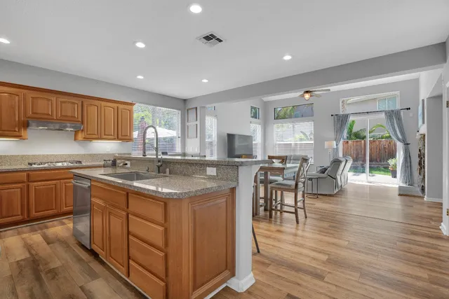 a kitchen with stainless steel appliances granite countertop wooden cabinets a sink a stove a dining table and chairs