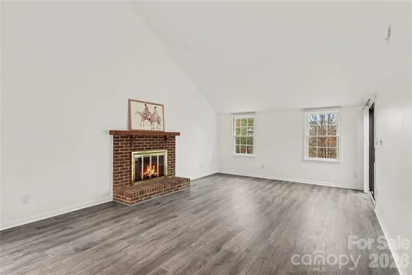 an empty room with wooden floor fireplace and windows