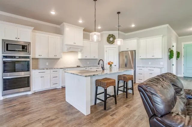 a kitchen with stainless steel appliances granite countertop a stove a sink a refrigerator and a dining table with wooden floor