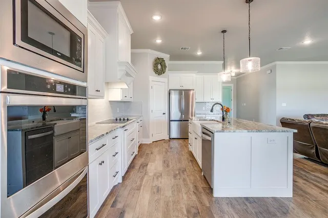 a large kitchen with stainless steel appliances kitchen island granite countertop a stove a sink dishwasher and a refrigerator with wooden floor