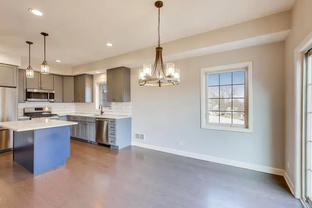 a open kitchen with stainless steel appliances granite countertop a sink dishwasher a stove a refrigerator and a dining table with wooden floor