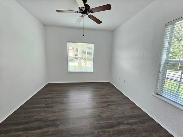 an empty room with wooden floor fan and windows