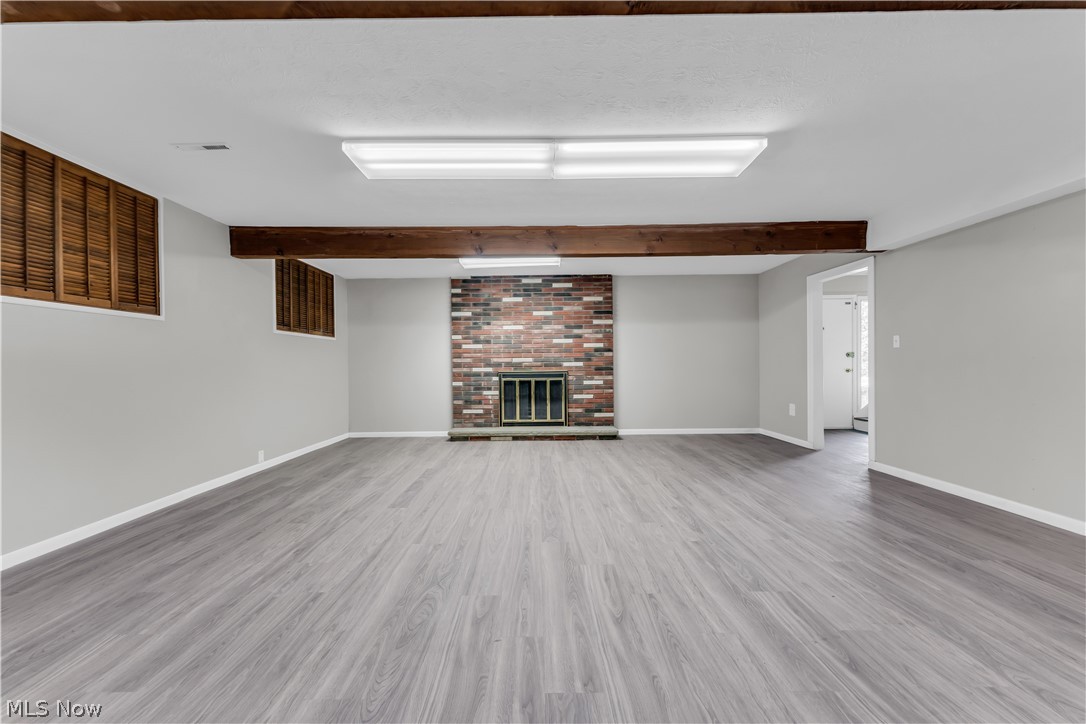 6190 Mill Road Broadview Heights, OH 44147 - Photo 23 of 36 Unfurnished living room with beamed ceiling, brick wall, a brick fireplace, and hardwood / wood-style floors