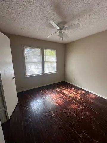an empty room with wooden floor fan and windows