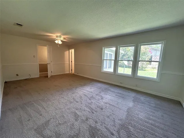 an empty room with chandelier fan and windows