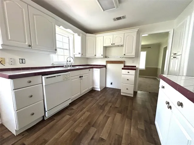 a large white kitchen with granite countertop a stove top oven a sink dishwasher and white cabinets with wooden floor