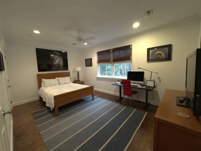 a bedroom with a bed a computer on desk and a dresser with wooden floor