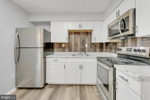 a kitchen with stainless steel appliances granite countertop a refrigerator a stove a sink and white cabinets with wooden floor