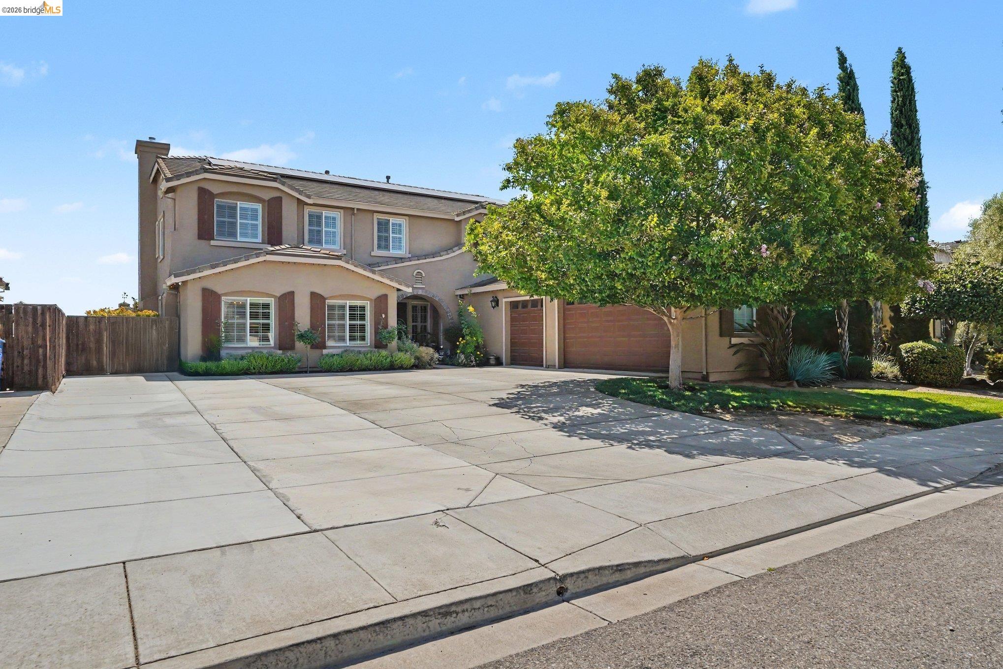 106 Little Ranch Circle Oakley, CA 94561 - Photo 32 of 34 Stucco exterior residence featuring shuttered windows, a two-car garage with wood-finish doors, and a mature tree providing shade