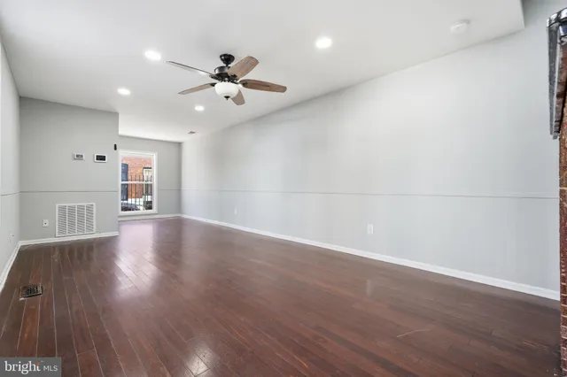 a view of an empty room with wooden floor and a ceiling fan