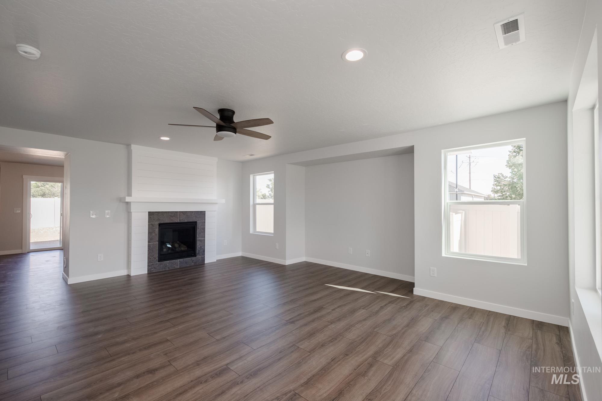3270 West Morere Drive Meridian, ID 83642 - Photo 10 of 26 Unfurnished living room with healthy amount of natural light, dark wood-style floors, a ceiling fan, a tile fireplace, and recessed lighting