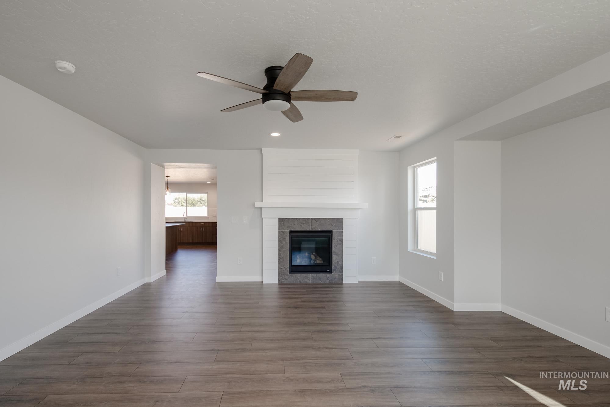 3270 West Morere Drive Meridian, ID 83642 - Photo 12 of 26 Unfurnished living room featuring dark wood-style floors, a ceiling fan, a tiled fireplace, and recessed lighting