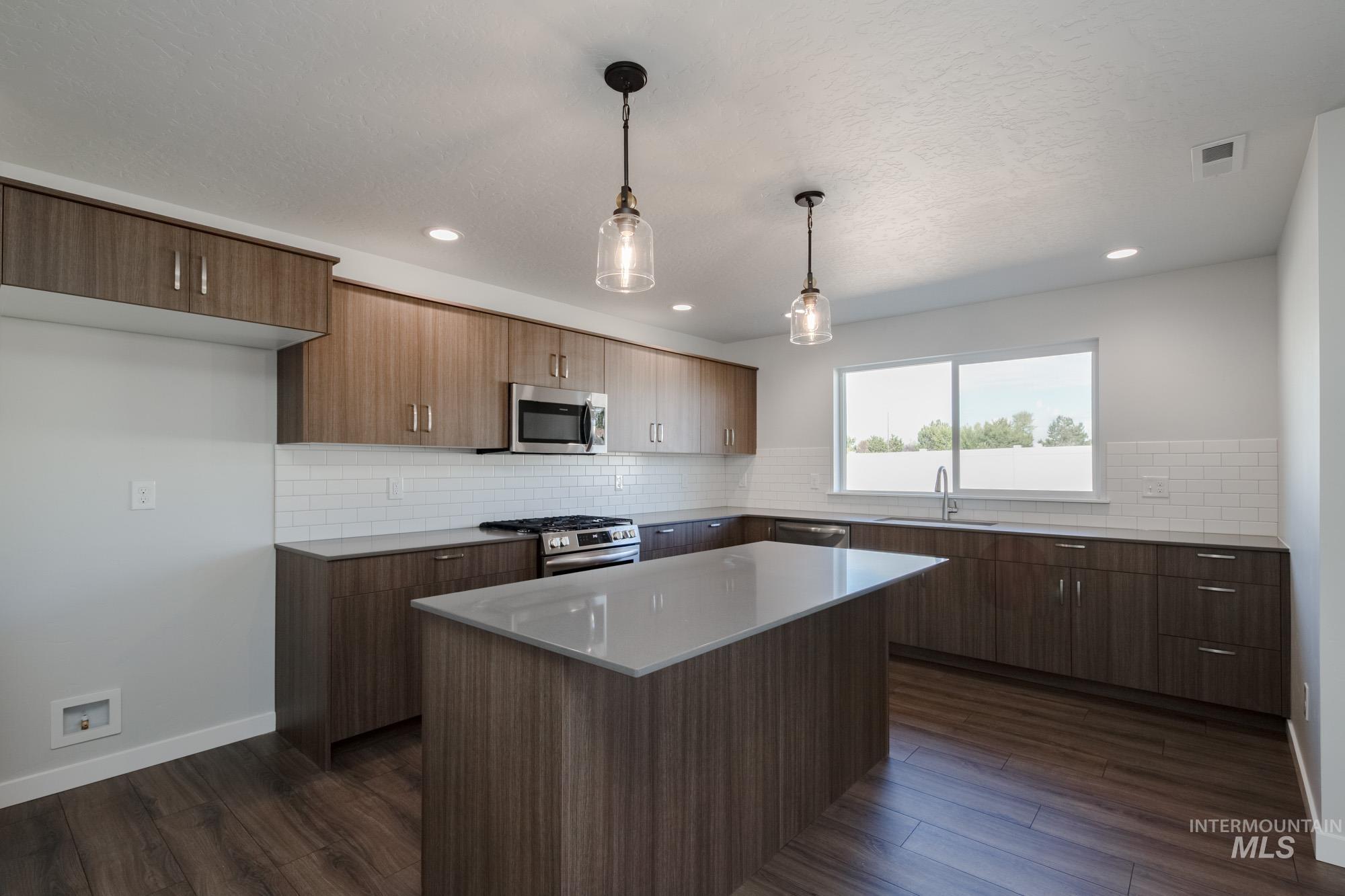 3270 West Morere Drive Meridian, ID 83642 - Photo 5 of 26 Kitchen with decorative light fixtures, dark wood-style flooring, appliances with stainless steel finishes, a kitchen island, and recessed lighting