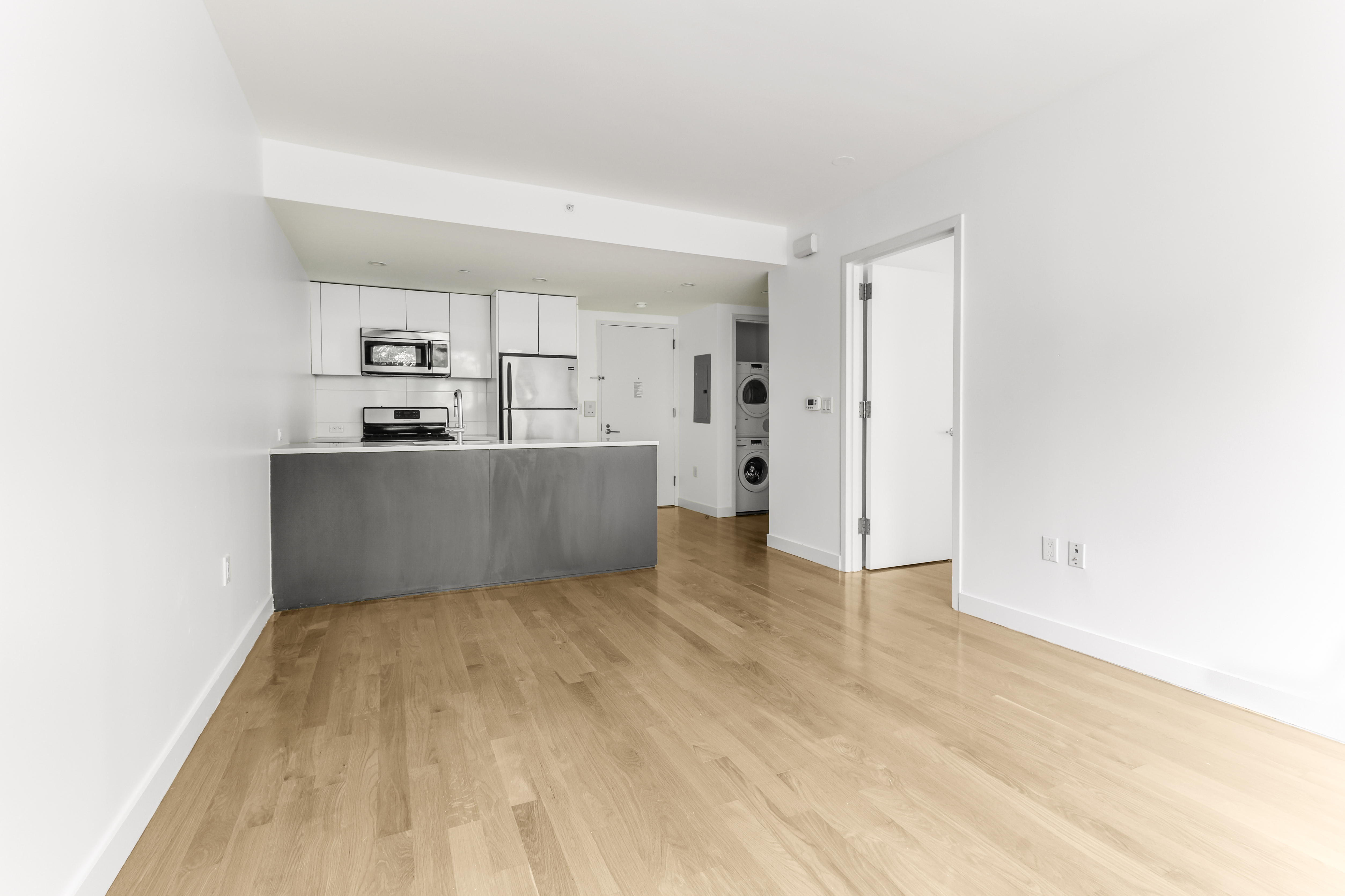 a view of kitchen and empty room with wooden floor