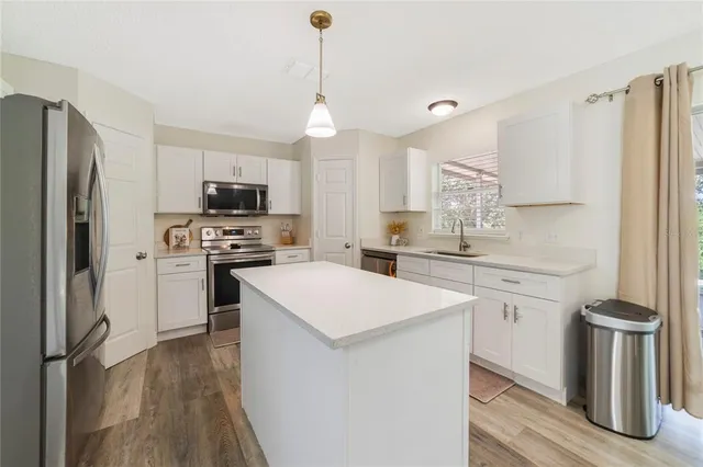 a kitchen with a refrigerator a stove a sink and white cabinets with wooden floor